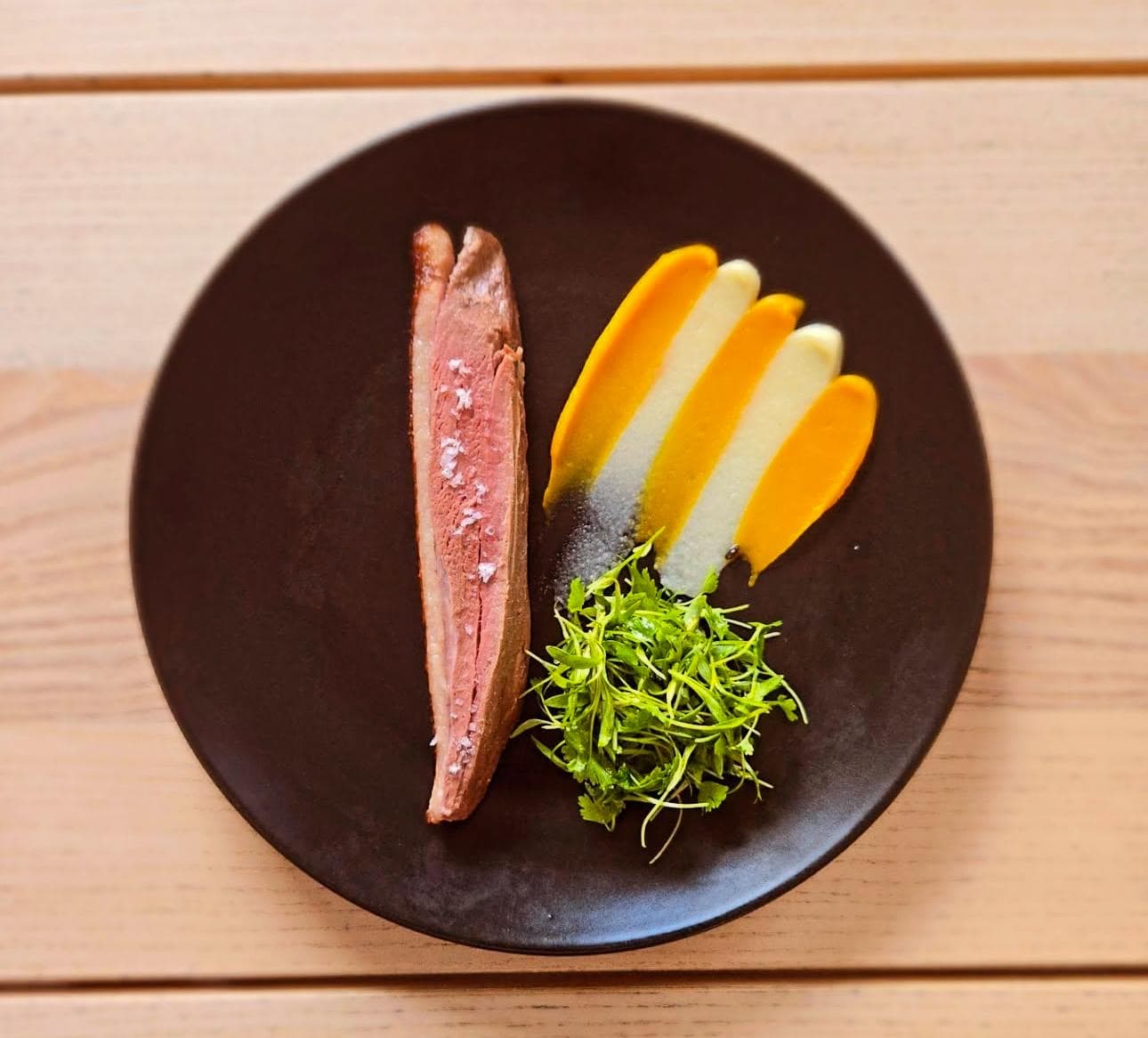 Plato de carne con purés de colores y hierbas frescas en Estela